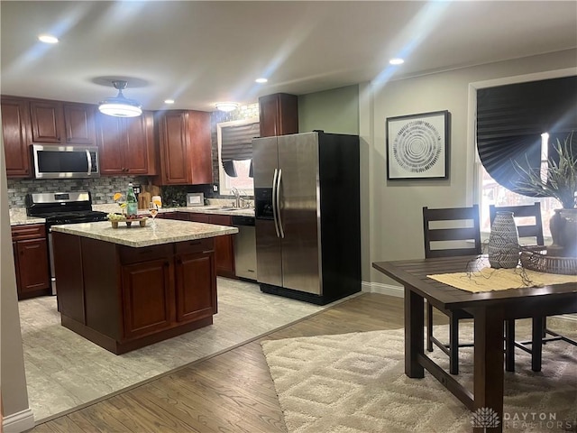 kitchen with light wood-style flooring, a sink, a kitchen island, appliances with stainless steel finishes, and tasteful backsplash