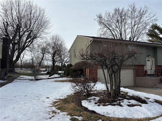 view of snowy exterior with an attached garage, fence, and brick siding