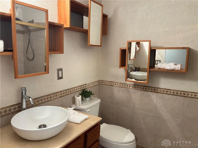 bathroom featuring a textured wall, toilet, a wainscoted wall, vanity, and tile walls