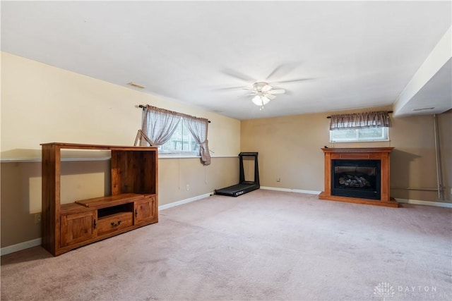 unfurnished living room featuring visible vents, a glass covered fireplace, light carpet, ceiling fan, and baseboards