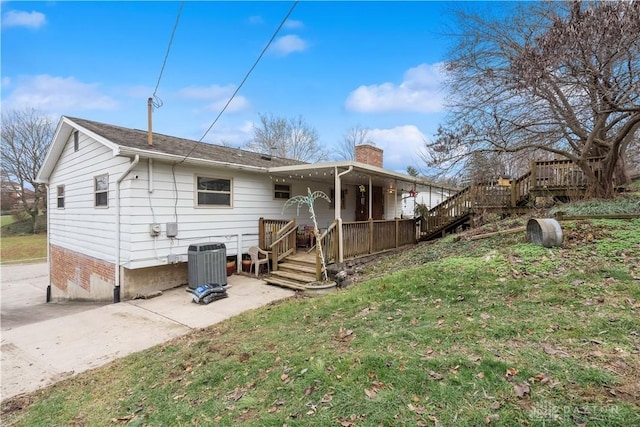 rear view of house with a wooden deck, a chimney, cooling unit, and a lawn