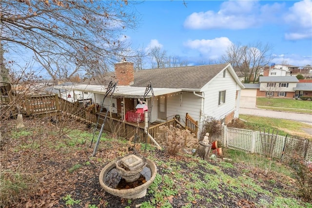 back of property with a shingled roof, driveway, fence, and a chimney