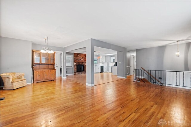 unfurnished living room featuring an inviting chandelier, a fireplace, and light hardwood / wood-style floors