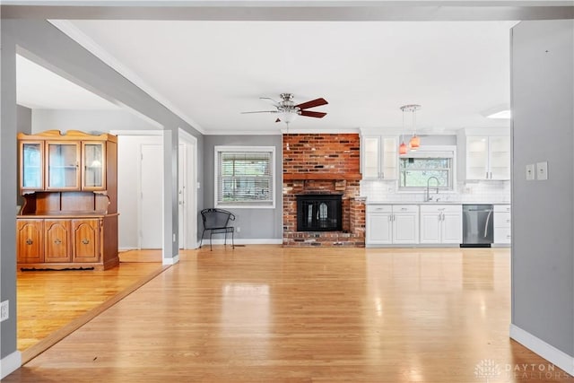 unfurnished living room with a healthy amount of sunlight, sink, a brick fireplace, and light wood-type flooring