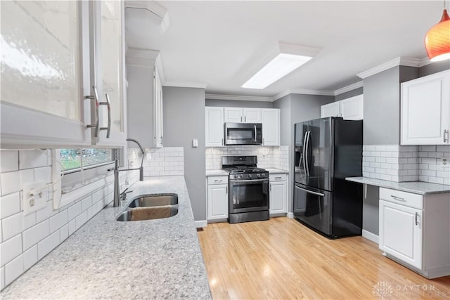 kitchen with crown molding, appliances with stainless steel finishes, white cabinets, a sink, and light wood-type flooring