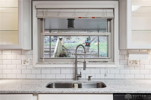 room details with dishwashing machine, light stone countertops, sink, and white cabinets