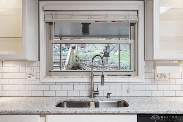 kitchen featuring backsplash, glass insert cabinets, white cabinets, a sink, and dishwashing machine