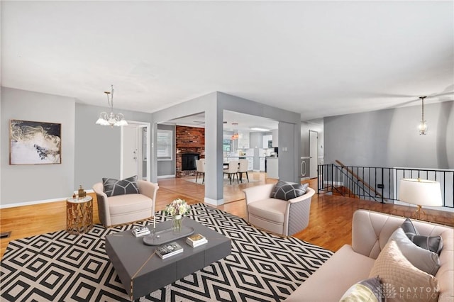 living area featuring a brick fireplace, baseboards, a notable chandelier, and wood finished floors