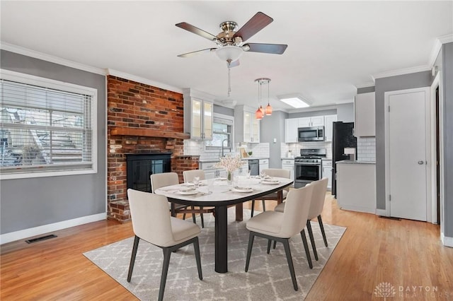 dining area with visible vents, ornamental molding, a brick fireplace, and light wood-style flooring