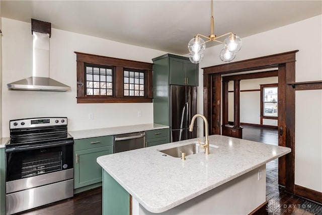 kitchen featuring wall chimney exhaust hood, sink, appliances with stainless steel finishes, pendant lighting, and a kitchen island with sink