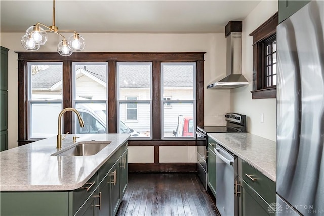 kitchen with sink, decorative light fixtures, an island with sink, stainless steel appliances, and wall chimney range hood