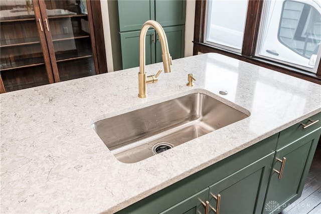 details featuring light stone counters, sink, and green cabinetry