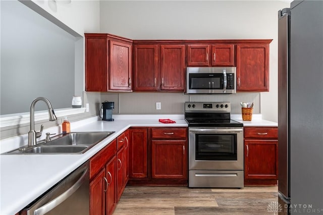 kitchen with stainless steel appliances, sink, and light hardwood / wood-style flooring