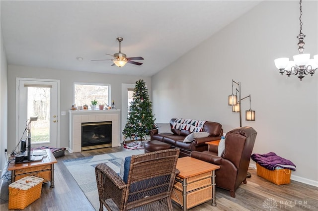 living room featuring a tiled fireplace, vaulted ceiling, dark wood-type flooring, and ceiling fan with notable chandelier