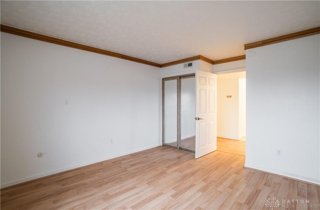 unfurnished bedroom featuring light hardwood / wood-style flooring, ornamental molding, and a closet