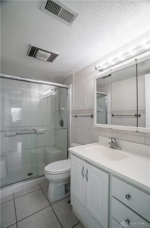 bathroom with tile walls, vanity, an enclosed shower, toilet, and a textured ceiling