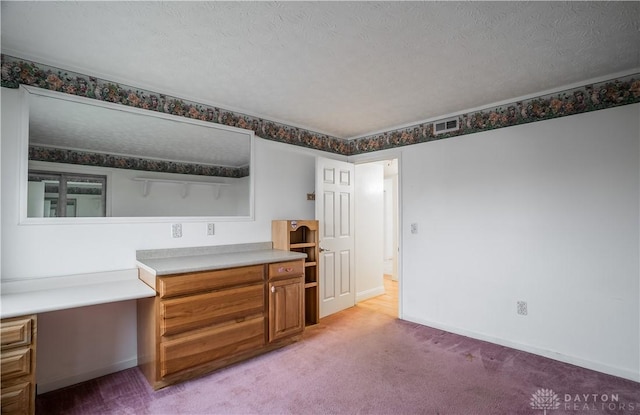 kitchen with built in desk, light colored carpet, and a textured ceiling