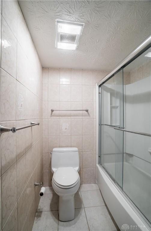 bathroom with combined bath / shower with glass door, tile walls, tile patterned flooring, a textured ceiling, and toilet