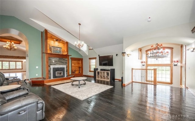 living room with an inviting chandelier, dark hardwood / wood-style floors, a stone fireplace, and vaulted ceiling