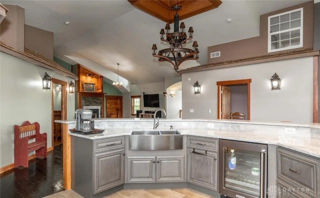 kitchen with gray cabinets, sink, wine cooler, light stone countertops, and an inviting chandelier