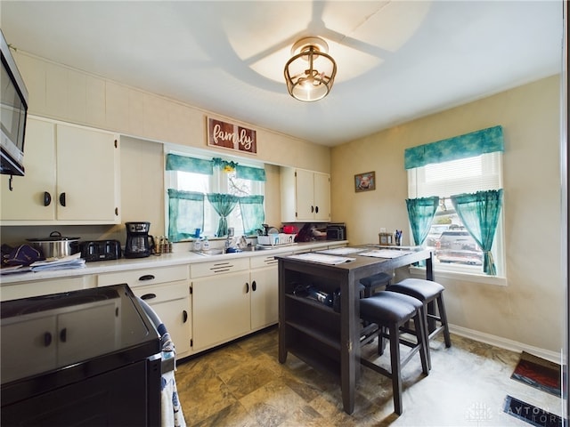 kitchen with black electric range oven, sink, and white cabinets