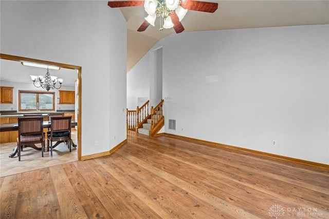 living room featuring lofted ceiling, ceiling fan with notable chandelier, and light hardwood / wood-style flooring