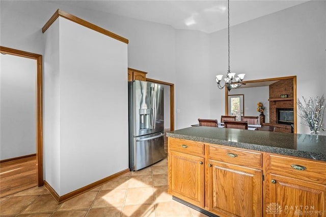 kitchen featuring pendant lighting, light tile patterned floors, stainless steel refrigerator with ice dispenser, a brick fireplace, and an inviting chandelier