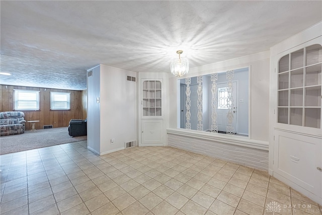 spare room featuring a textured ceiling, light tile patterned flooring, wood walls, and a notable chandelier