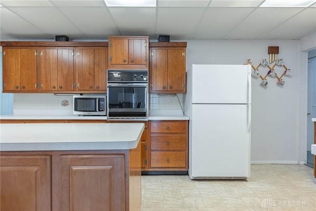 kitchen featuring white fridge, tasteful backsplash, black oven, and a drop ceiling