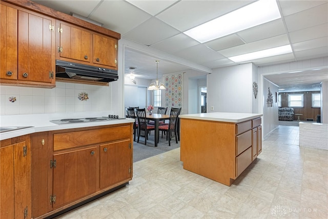 kitchen featuring white cooktop, a drop ceiling, decorative light fixtures, decorative backsplash, and a kitchen island