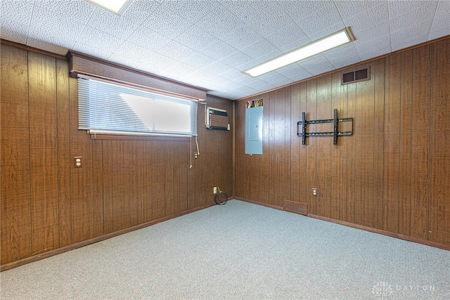 carpeted empty room featuring electric panel, a wall mounted AC, and wood walls