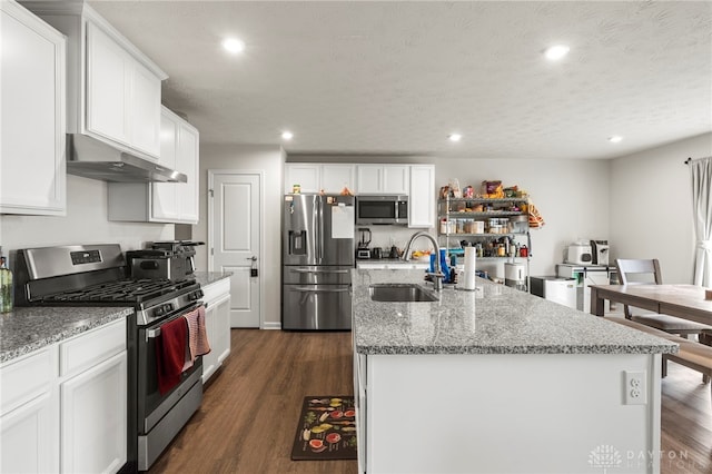 kitchen with appliances with stainless steel finishes, white cabinetry, an island with sink, sink, and light stone counters