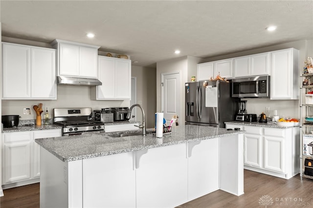 kitchen with light stone counters, stainless steel appliances, an island with sink, and white cabinets