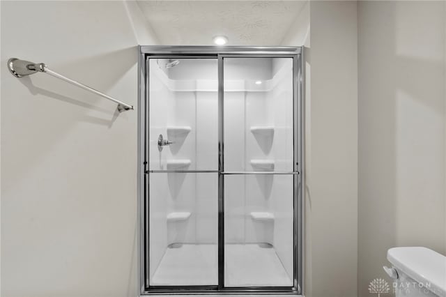 bathroom with toilet, a shower with door, and a textured ceiling