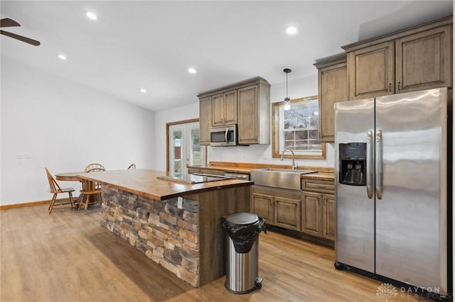 kitchen featuring sink, butcher block countertops, appliances with stainless steel finishes, pendant lighting, and light hardwood / wood-style floors