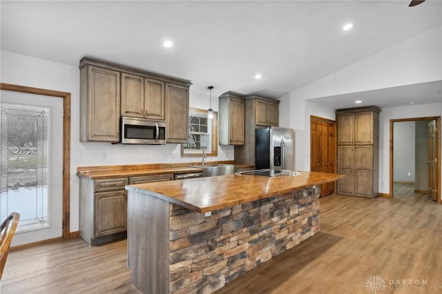 kitchen featuring butcher block countertops, vaulted ceiling, light hardwood / wood-style flooring, appliances with stainless steel finishes, and pendant lighting