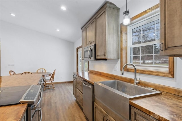 kitchen featuring wood counters, sink, hanging light fixtures, light wood-type flooring, and appliances with stainless steel finishes