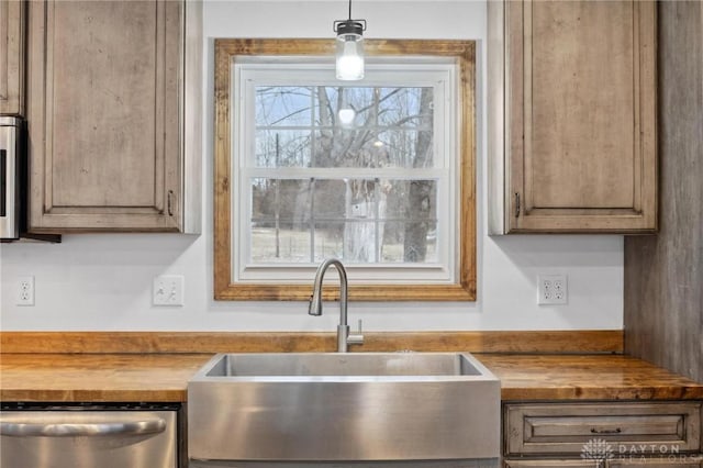 kitchen featuring wood counters, sink, stainless steel dishwasher, and hanging light fixtures