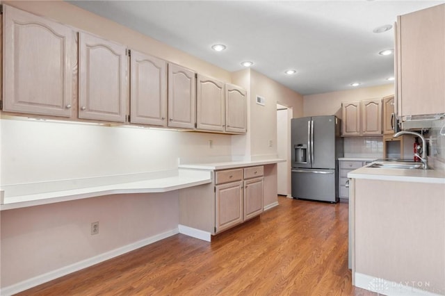 kitchen featuring sink, wood-type flooring, built in desk, stainless steel fridge with ice dispenser, and decorative backsplash