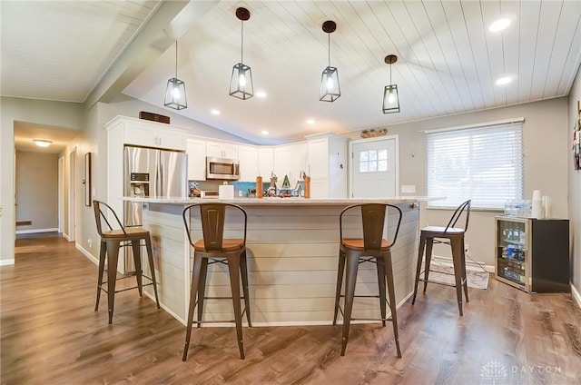 bar with white cabinetry, lofted ceiling, hanging light fixtures, hardwood / wood-style flooring, and stainless steel appliances