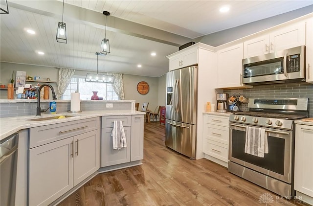 kitchen with sink, hanging light fixtures, hardwood / wood-style flooring, stainless steel appliances, and white cabinets