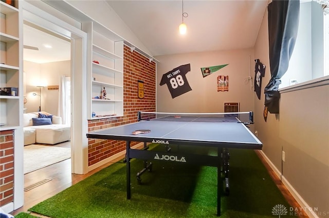 playroom featuring lofted ceiling, brick wall, and hardwood / wood-style floors