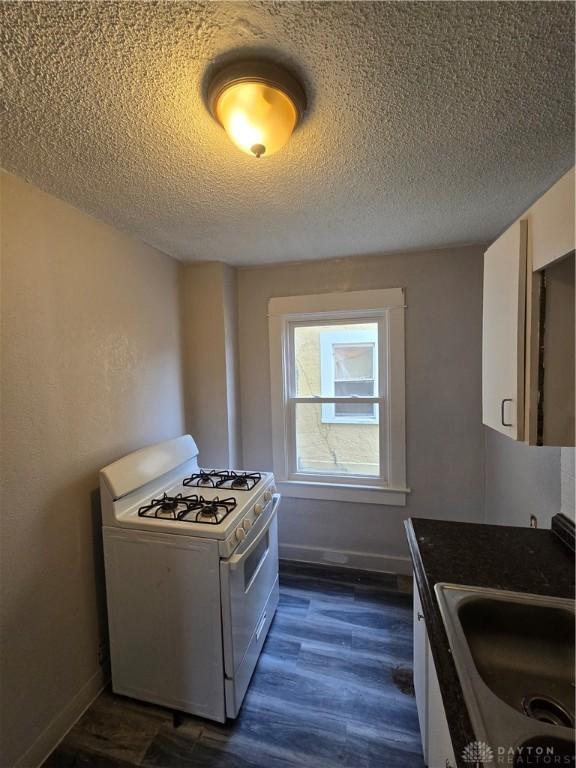 kitchen featuring sink, gas range gas stove, dark hardwood / wood-style floors, a textured ceiling, and white cabinets