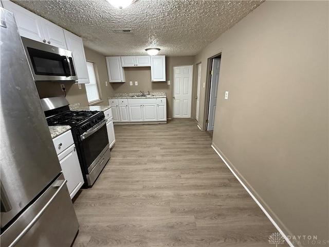 kitchen with sink, appliances with stainless steel finishes, white cabinetry, a textured ceiling, and light wood-type flooring