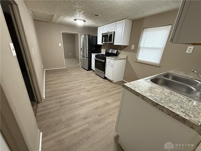 kitchen with sink, a textured ceiling, light wood-type flooring, stainless steel appliances, and white cabinets