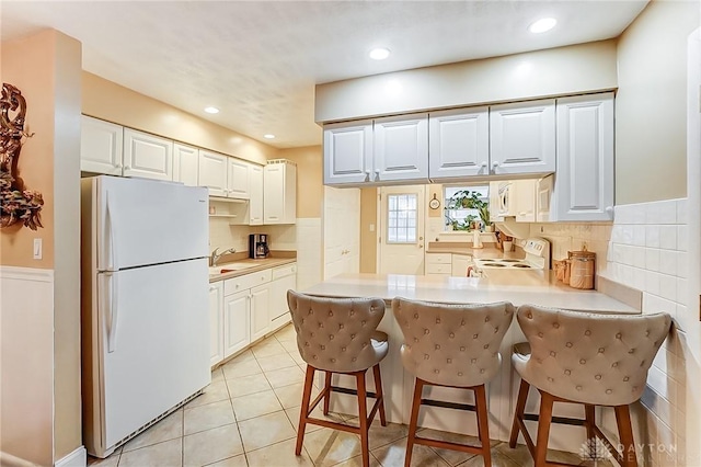 kitchen featuring white cabinetry, a kitchen bar, and white appliances