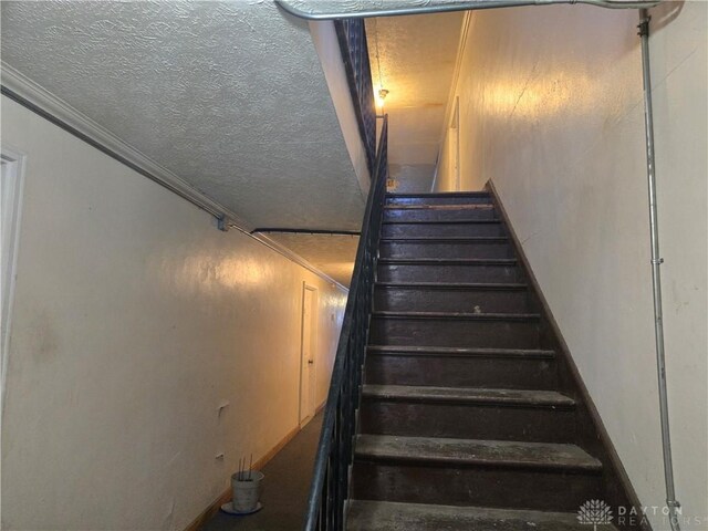 staircase featuring crown molding and a textured ceiling