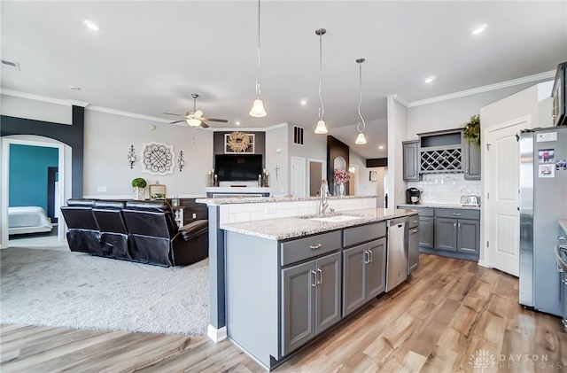 kitchen featuring stainless steel appliances, decorative light fixtures, sink, and a center island with sink