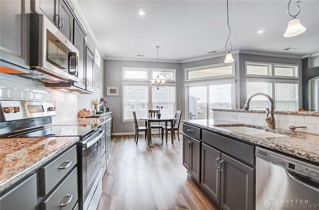 kitchen featuring sink, crown molding, light stone counters, appliances with stainless steel finishes, and pendant lighting