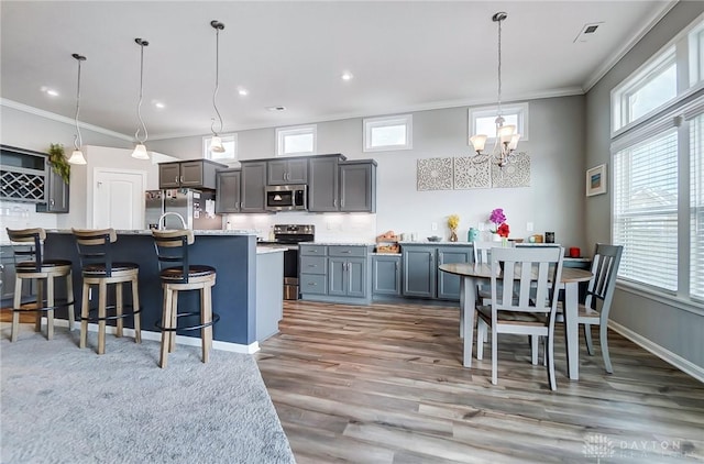 kitchen with pendant lighting, crown molding, a kitchen island with sink, stainless steel appliances, and tasteful backsplash